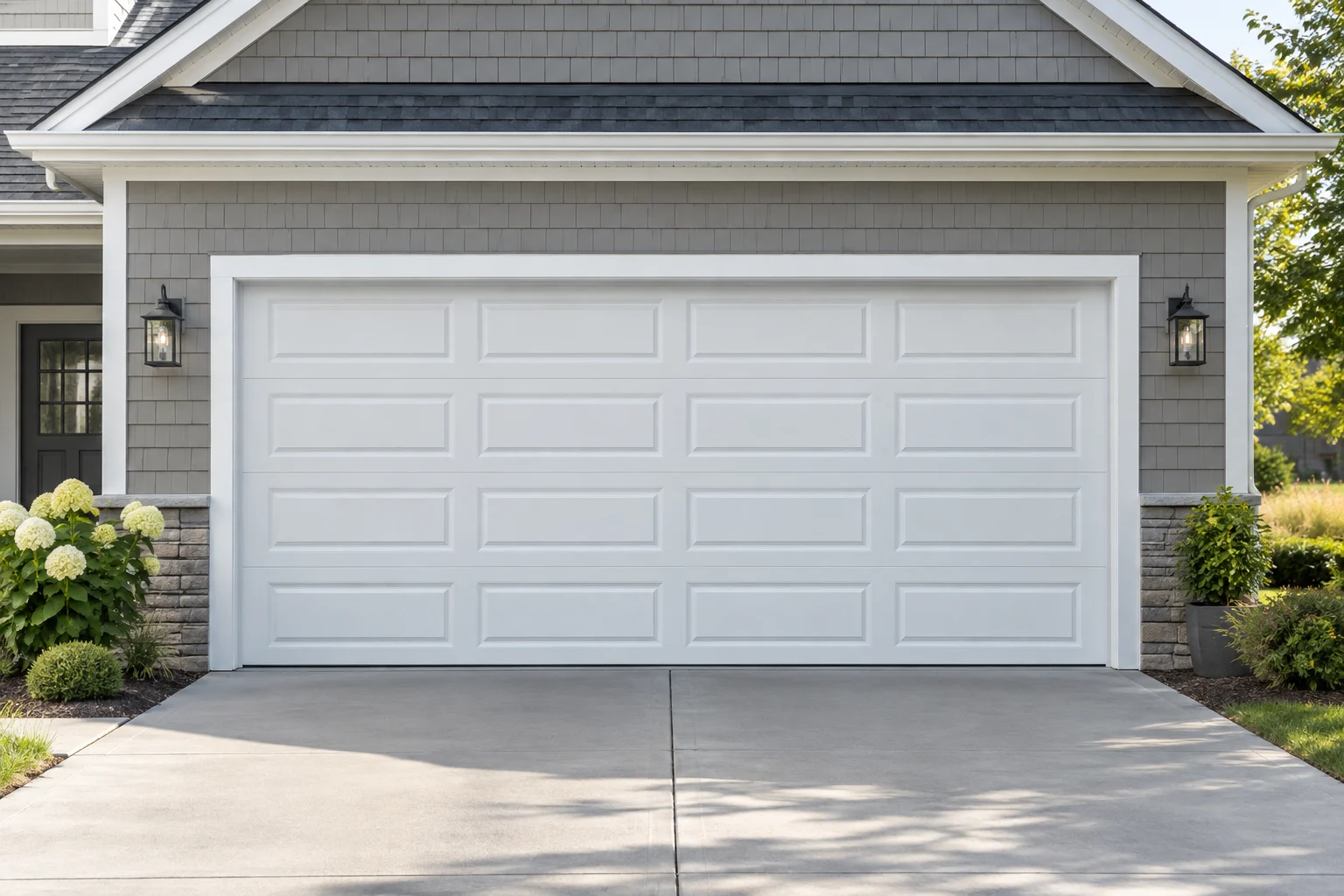 White raised-panel steel garage door on a gray shingle home in bright daylight